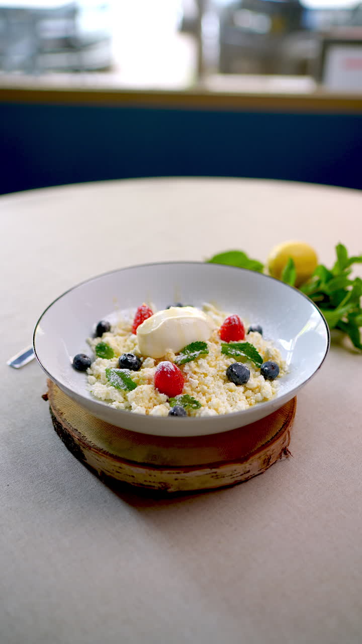 Delicious Eastern European cuisine dessert made with sweet cheese, honey, blueberries, raspberries, and mint, served on a white plate on a wooden base