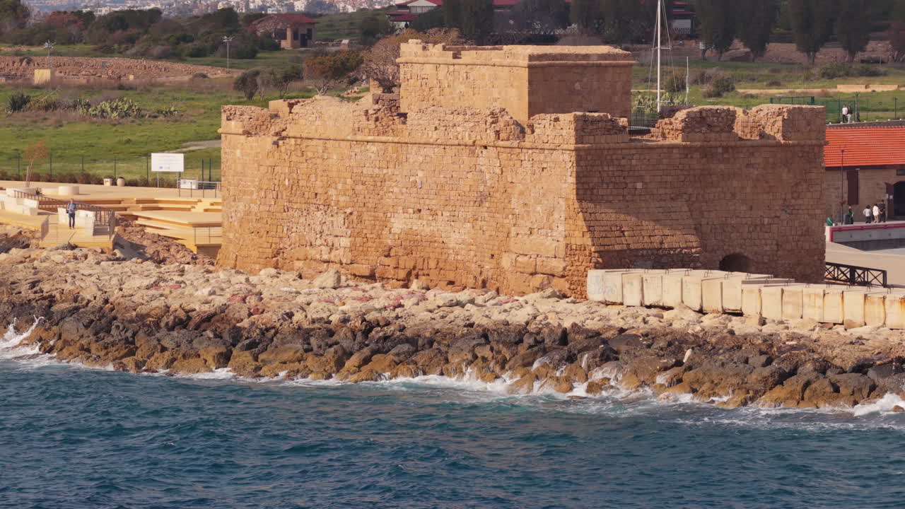 Vista aérea con dron de un castillo de piedra histórico ubicado en una costa rocosa con olas en Pafos, Chipre