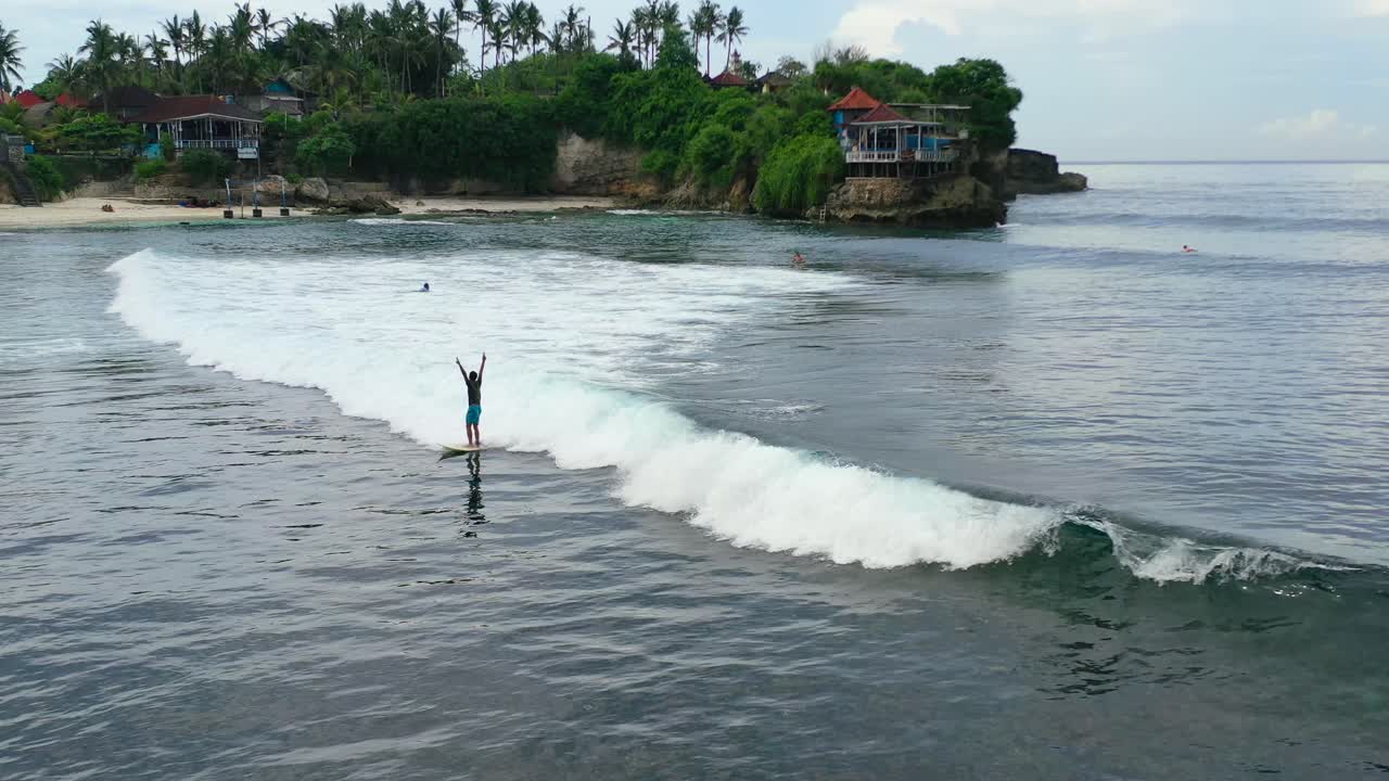 indonesian man catching an epic wave at Nusa Ceningan Island on cloudy day, aerial