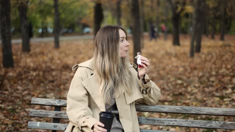 Frau-Trinkt-Kaffee-Zum-Mitnehmen-Und-Isst-Schokolade-Im-Herbstpark