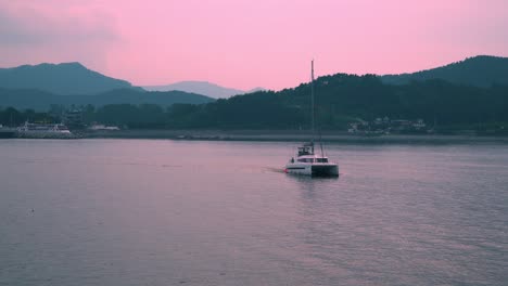 catamaran boat with tourists leisurely sailing at dusk with bright pink sky in south korea