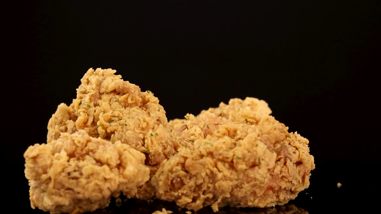 Golden, crispy fried chicken breasts and thighs rotate and zoom in slow motion against a black background, highlighting crunchy texture and spicy seasoning