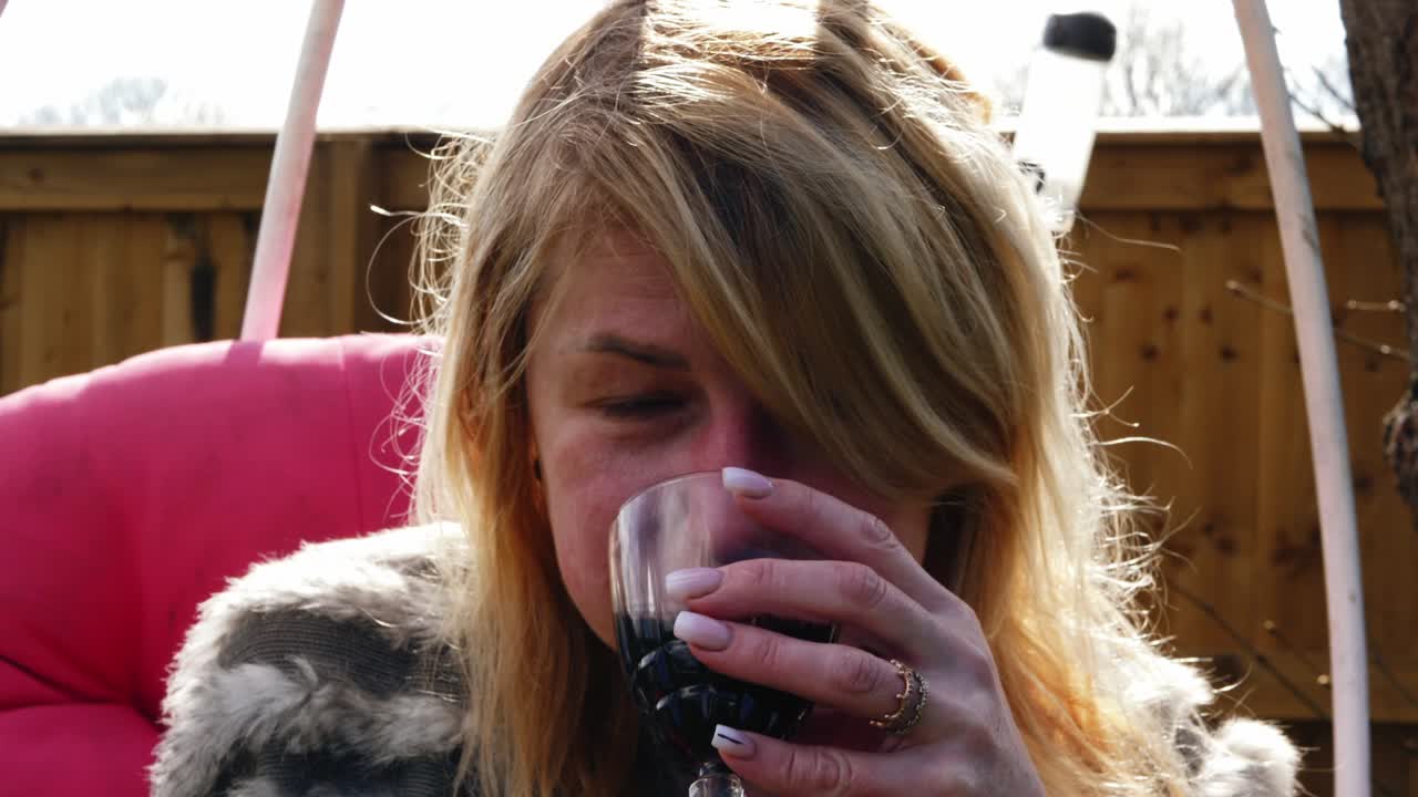 Attractive woman enjoys glass of wine in garden chair swing close up portrait 4k slow motion