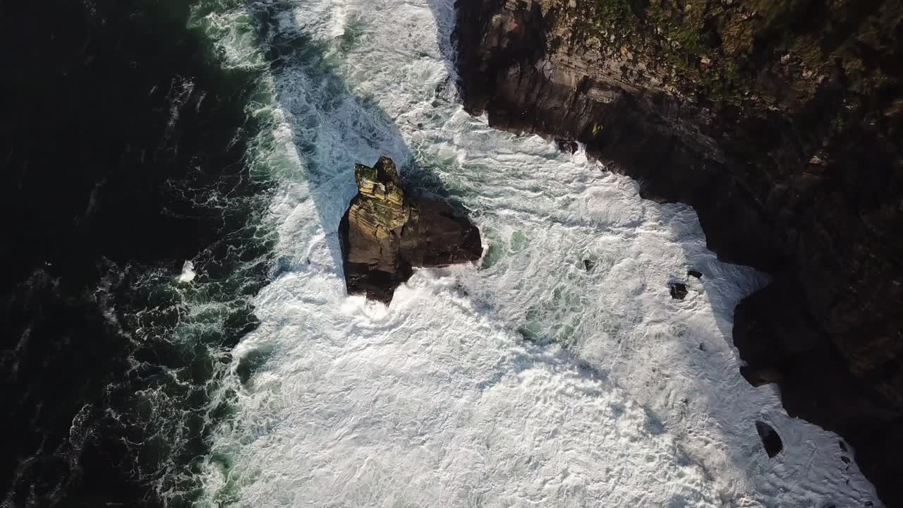 Rock next to the cliffs of Moher in the atlantic ocean, big waves create foam, drone aerial top view