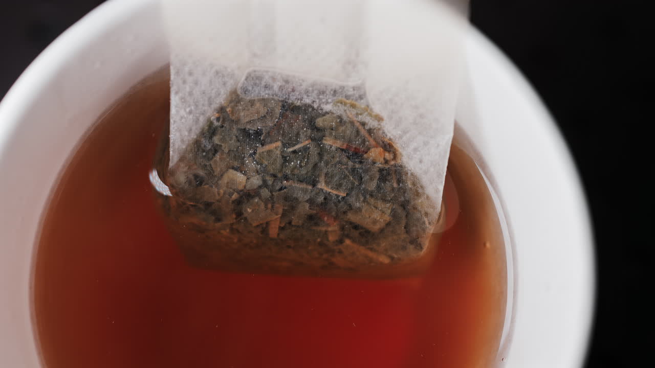 Close up of a tea bag steeping in hot water, releasing rich colour and aroma
