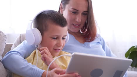 madre y hijo alegres en auriculares usando tableta