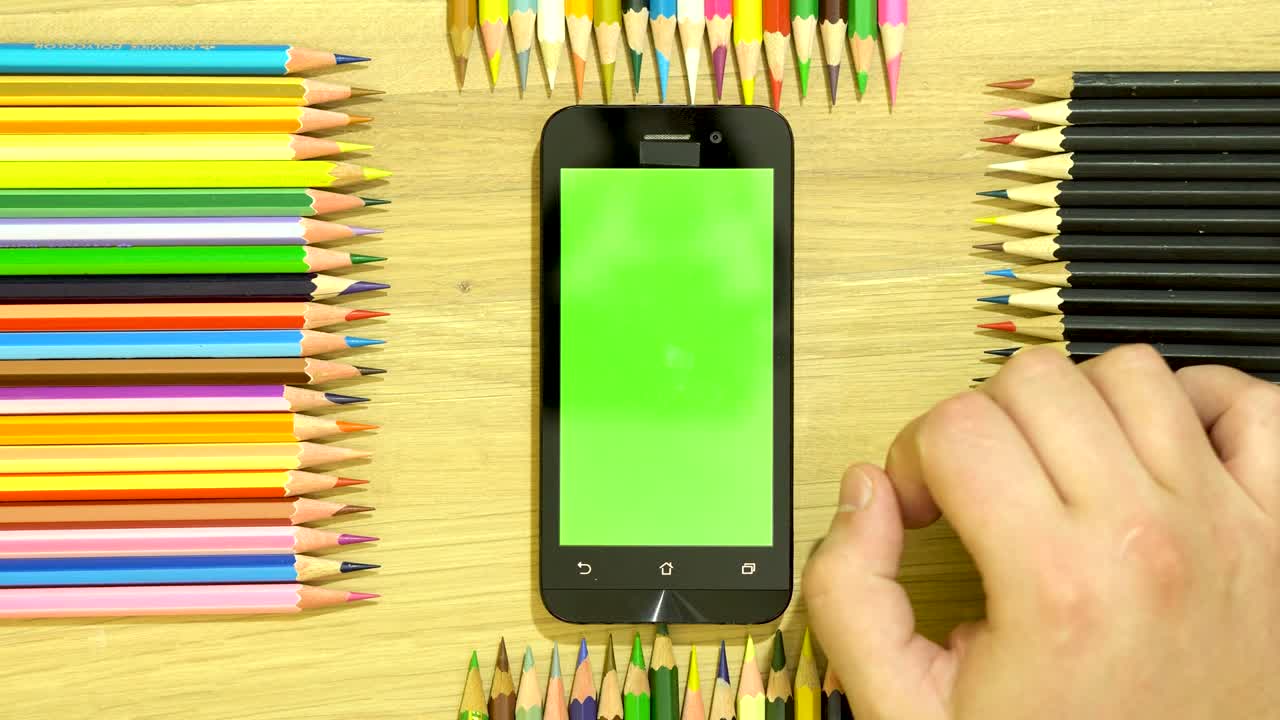 lápices de color en la mesa a lo largo del perímetro. mano en el teléfono inteligente.