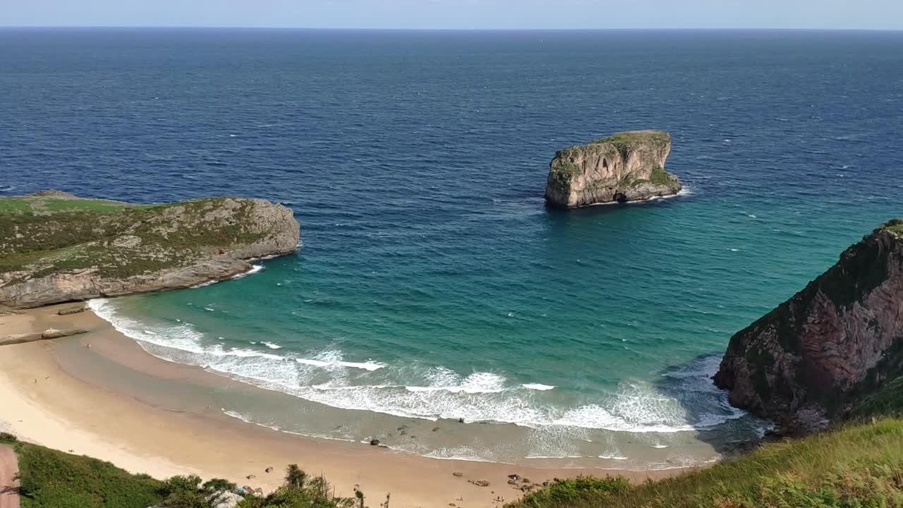 View of Ballota beach with turquoise waters and Castro Ballota Islet in Asturias
