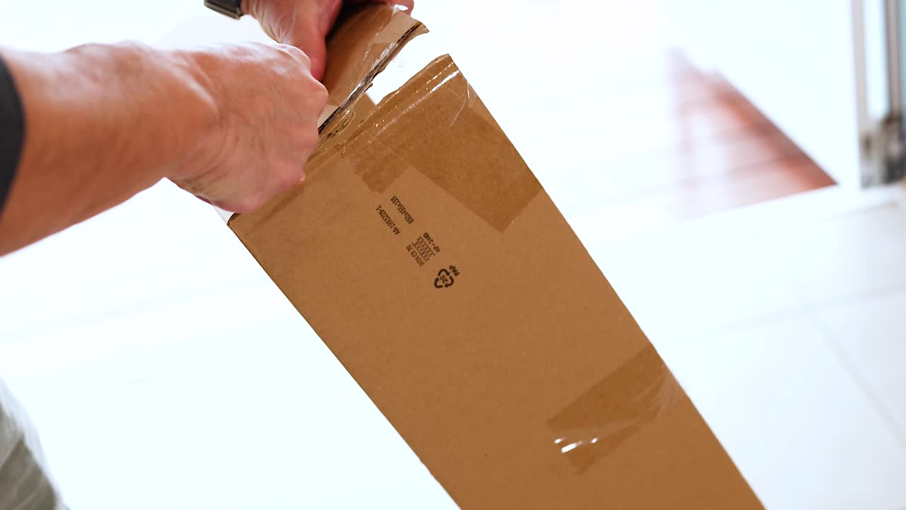 Hands carefully open a cardboard box using a knife in a well-lit room, highlighting precision and anticipation