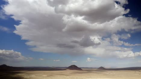 a descending aerial view of an empty and sun-scorched desert landscape with volcanic cones on an overcast day