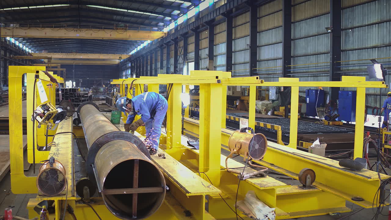Operaio di fabbrica che smeriglia un enorme tubo metallico industriale. Inquadratura media ampia