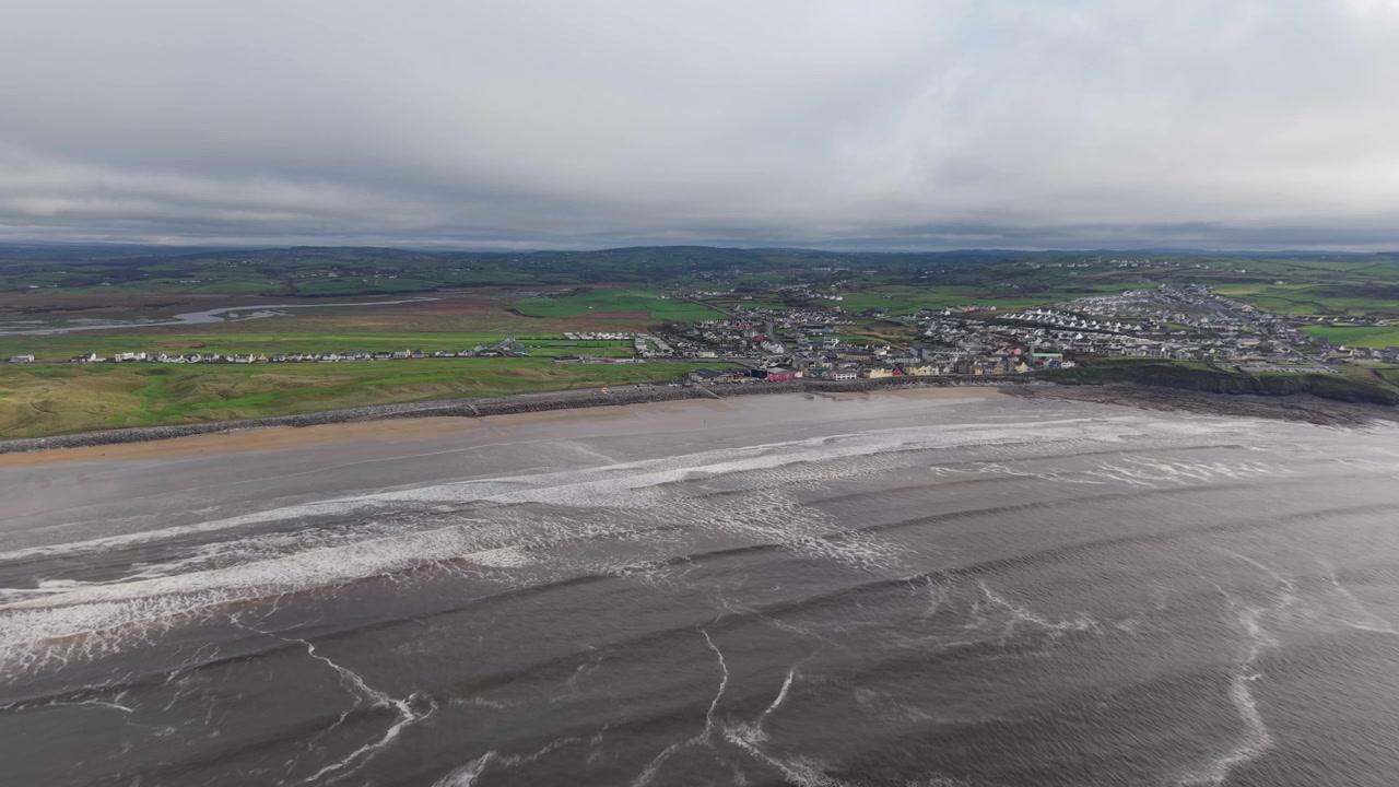 Vågor som slår in på Lahinch Beach med natursköna vyer över Cliffs of Moher på Irland