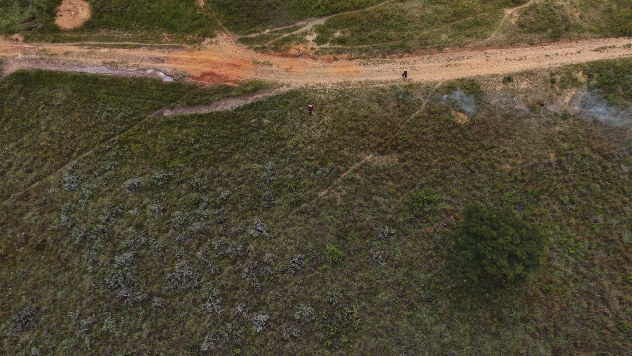 Aerial overhead footage showing controlled grassland ignition along dirt track