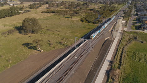 Train-drives-through-outer-suburbs-aerial-shot-rising