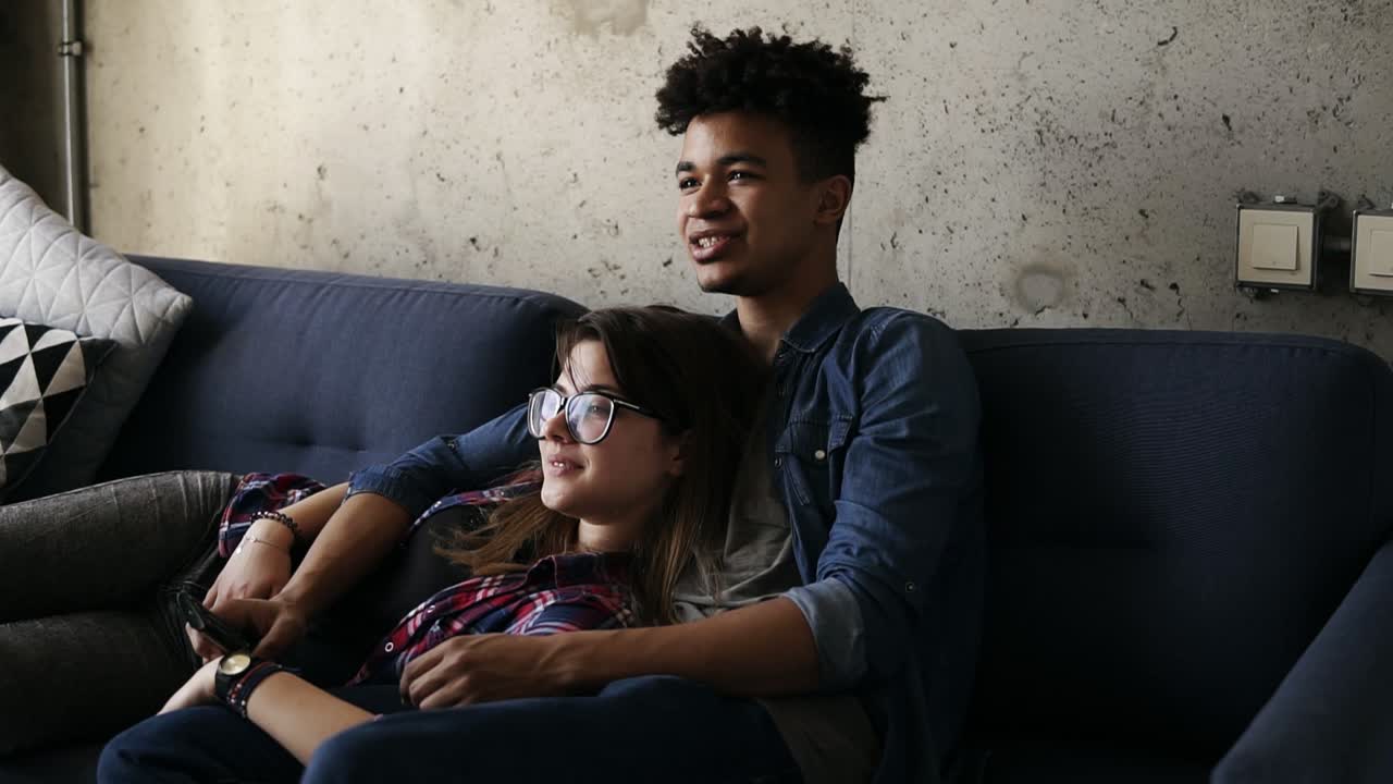 Cute happy couple of young hipsters lying on the couch, making silly faces,trying to find a perfect tv channel. Leisure time, enjoying youth, living together. Relationship goals.