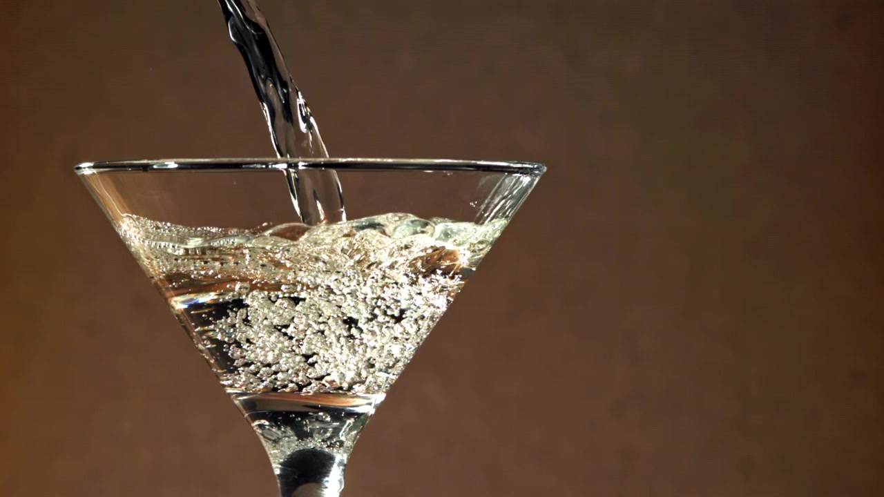 Liquido trasparente scintillante che si versa in un bicchiere da Martini