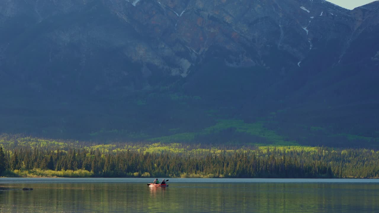 Due persone che praticano kayak panoramico sul lago Pyramid, che riflette montagne e foreste, nel Parco Nazionale Jasper, Canada.