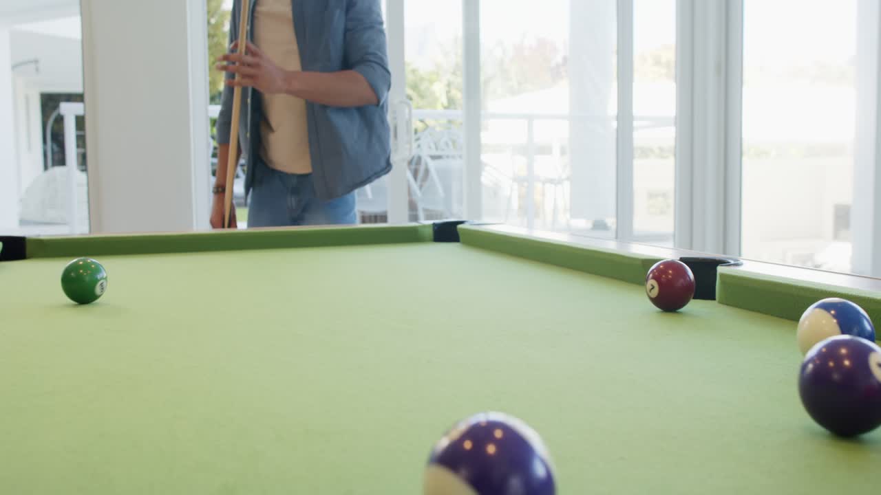 Upon entering frame, man by sliding glass door is breaking rack scattering balls at pool table