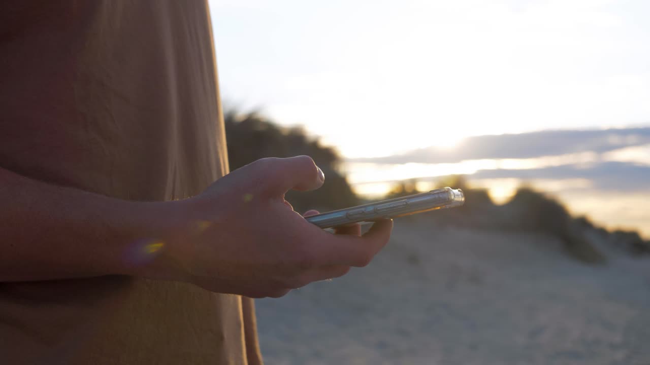 Giovane uomo con il telefono in mano sulla spiaggia al tramonto