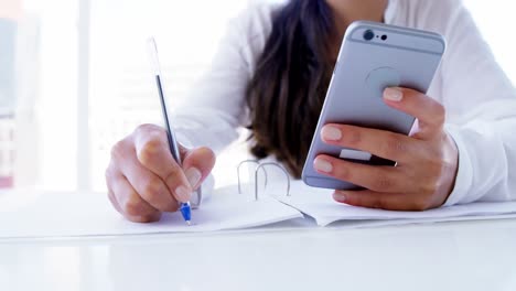 woman-using-smartphone-and-taking-notes