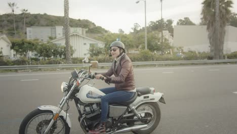 reveal of female biker who smiles at the camera while driving her vintage motorcycle in california