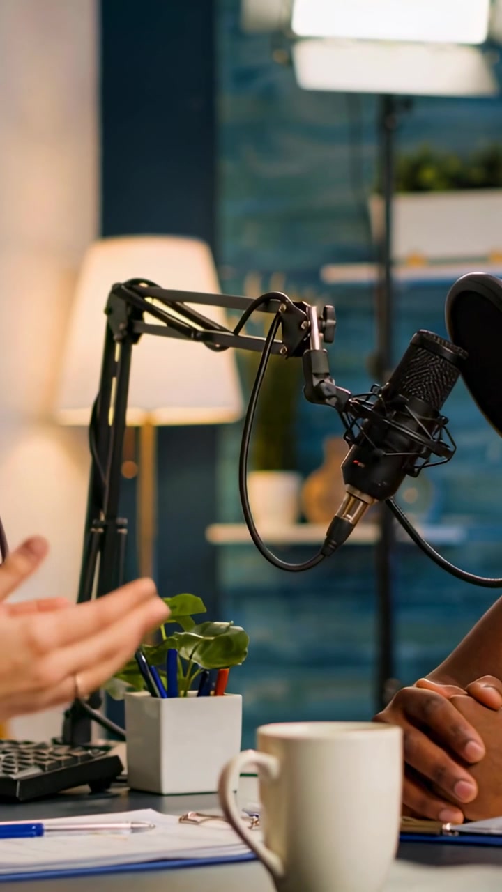 Venstre vært taler og gestikulerer til podcast, højre vært lytter, mikrofonens lydbølge reagerer på talen.