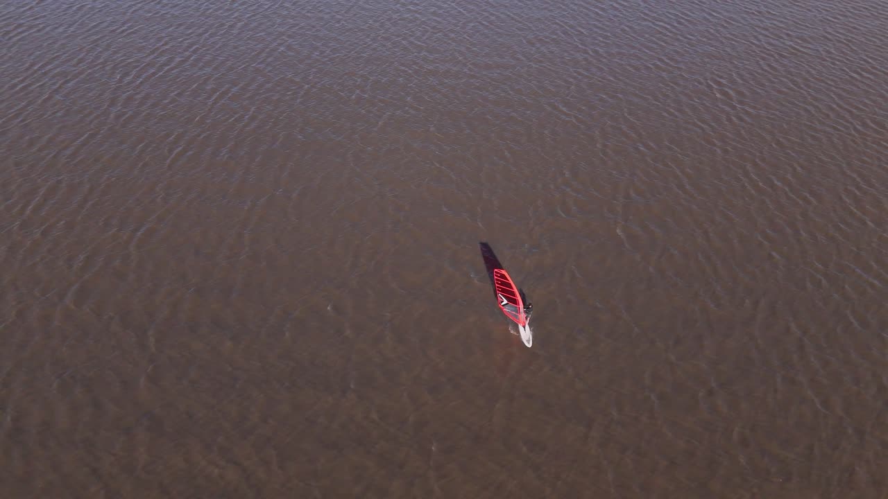Windsurfer glides on calm Rio De La Plata waters, peaceful and solo