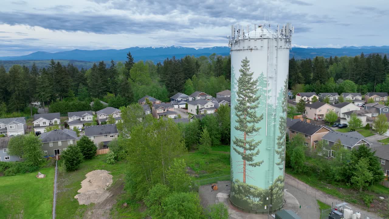 Záběr dronem na příměstskou vodárenskou věž s velkou nástěnnou malbou stromu na její straně.