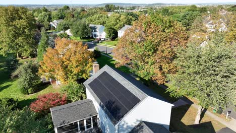 solar panels on roof of house in small american village at colorful autumn day. aerial top down landing shot. modern single family house with garden and colorful trees at sunny day.green energy theme.