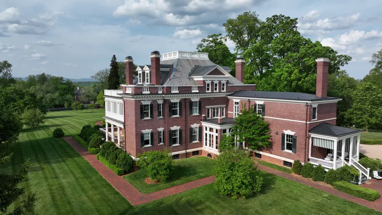 Majestic American mansion with classic brick facade and multiple chimneys, nestled in lush greenery. Elegant architecture with large windows and spacious lawn.Aerial view.