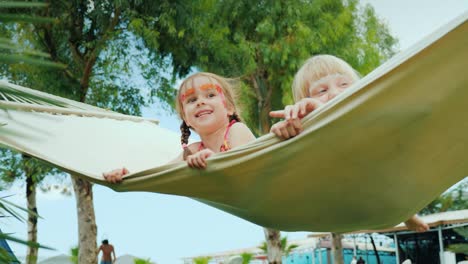 little children with aqua-grim on their faces skate happily on a white cloth hammock on the beautiful green glade of the hotel