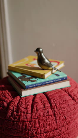 bird figurine on stack of books on a red pouf