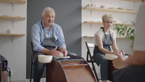 a group of senior women and a man together learn to make pottery on a potter's wheel. making utensils on a retired potter's wheel