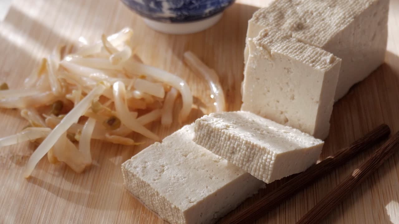 Soft tofu slices with bean sprouts and chopsticks on wooden board in natural light