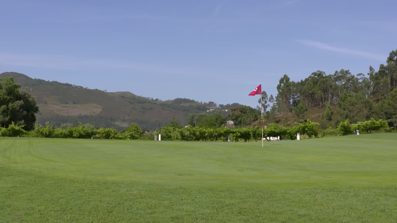 A view of the green and flag pole at a golf club, with mountains in the background