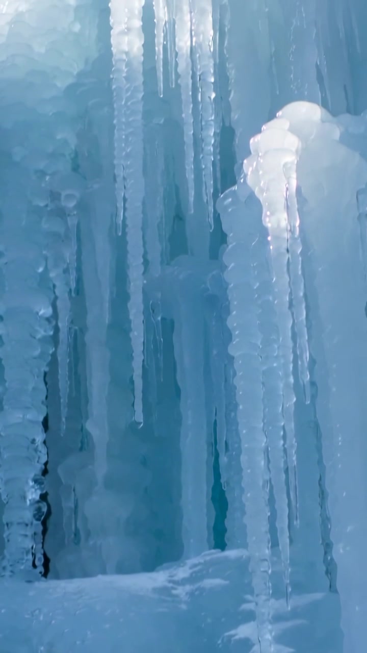 Vertical video: Tilting camera revealing vertical ice columns on cliff, showing sunlit icicle cap