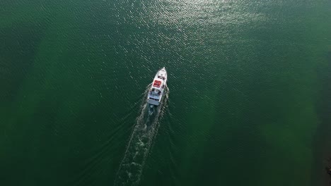 Aerial-top-down-tracking-follows-large-tourist-boat-driving-out-into-Caribbean-ocean-at-sunrise