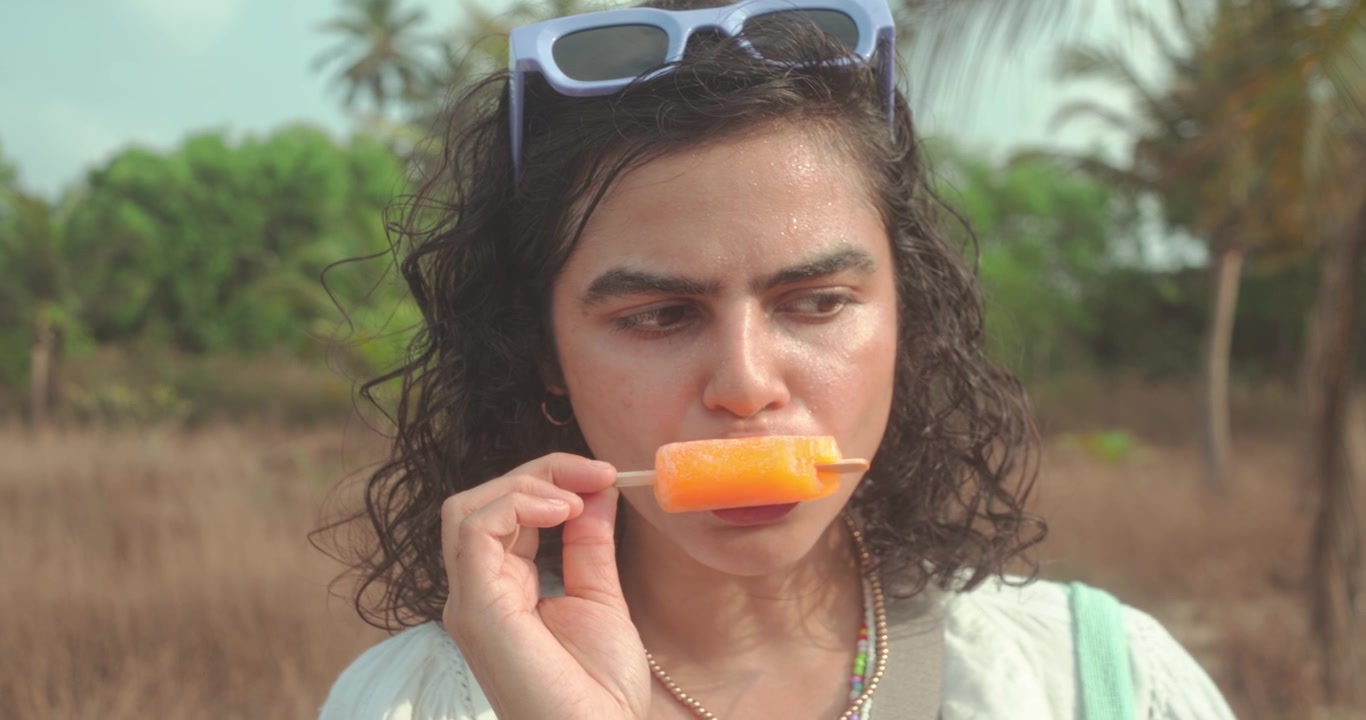 Primer plano de una mujer comiendo un polo de naranja bajo la cálida luz del sol, escena de estilo de vida veraniego relajado.