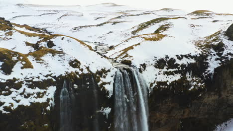 Aerial-pull-back-revealing-a-flock-of-birds-at-a-waterfall,-in-snowy-Iceland