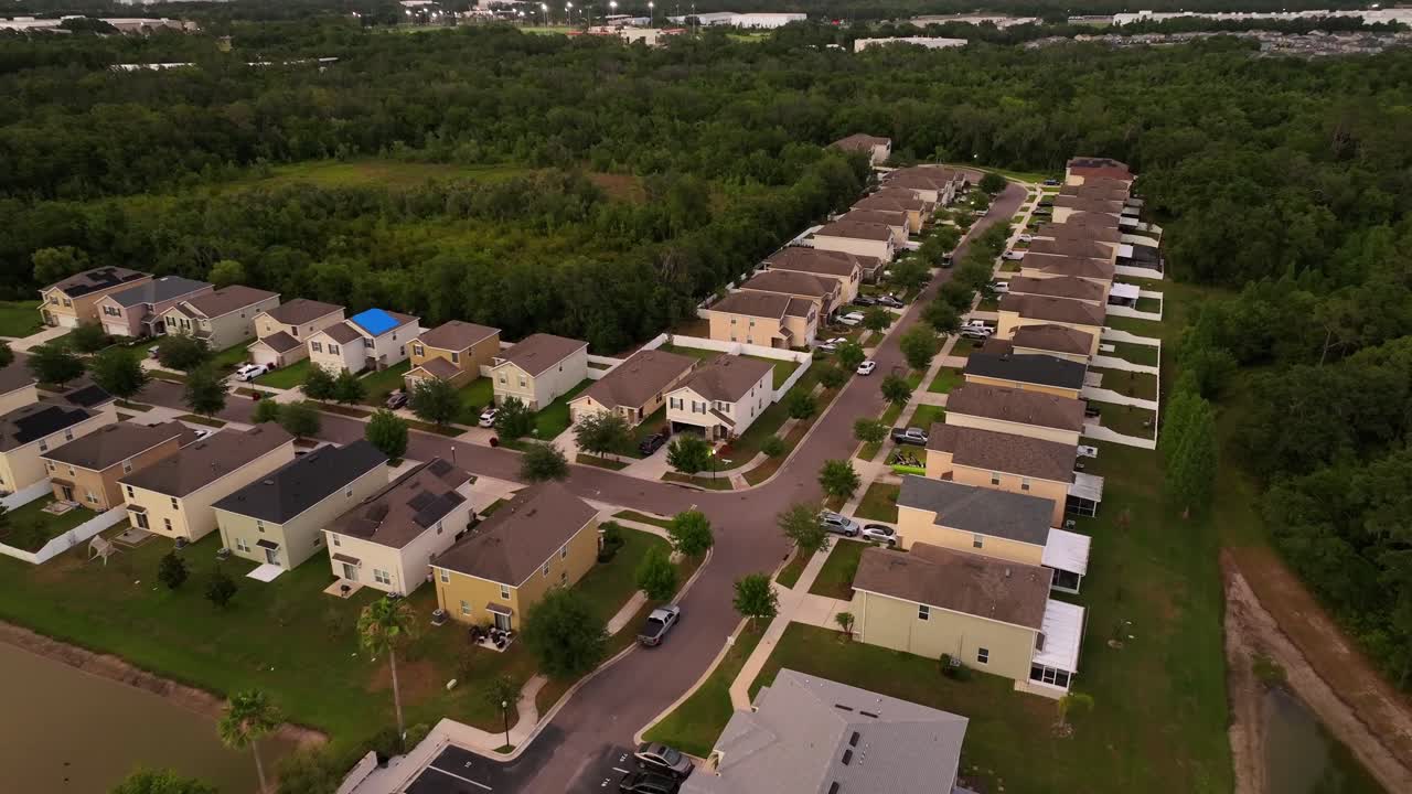 Aerial approaching shot of two-story houses with forest trees in suburb. Florida State during sunset time. Apartment and parking cars with palm trees. Wide shot. Luxury residential area of Brandon.