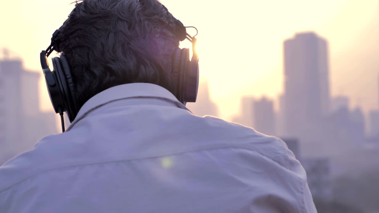 retrato de un joven con auriculares y escuchando música mientras el sol se pone en el fondo