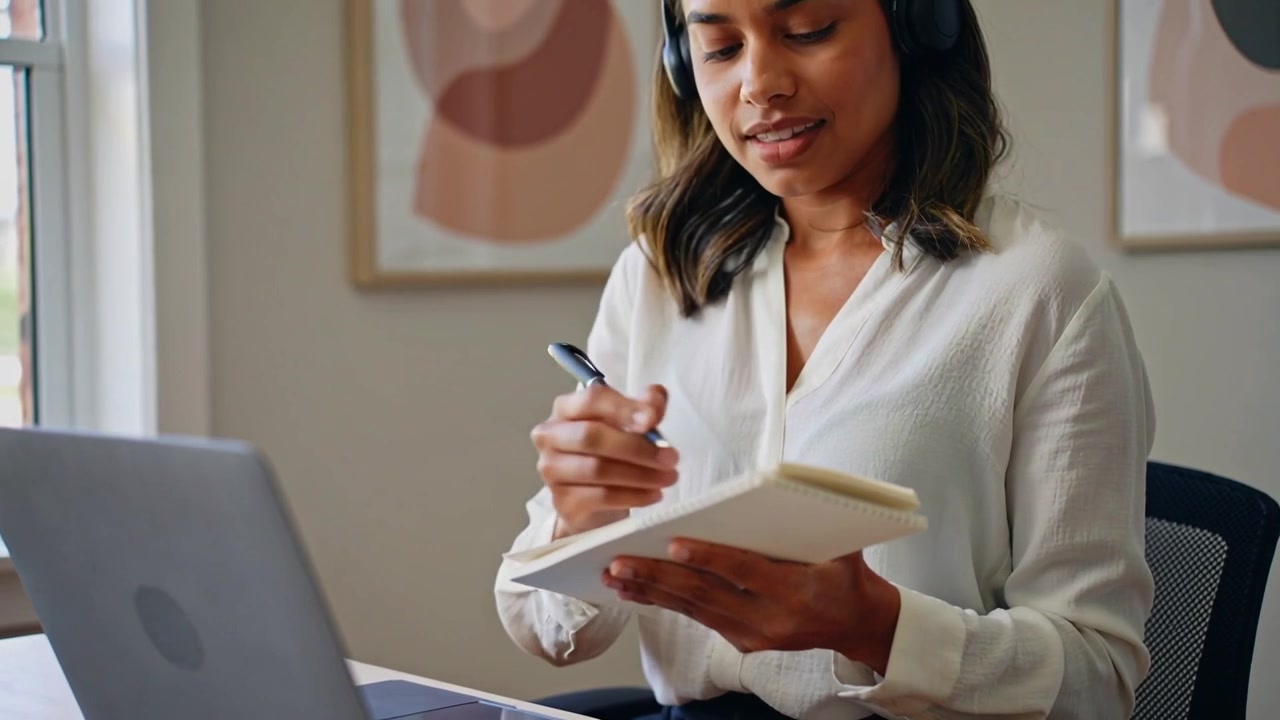 Starting tapping laptop trackpad at home, woman in white blouse taking notes from screen on notepad