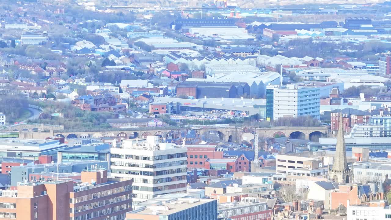 Panoramic cityscape of Sheffield shows a blend of modern towers, historic spires, and industrial warehouses across the urban landscape, captured in static aerial drone shot