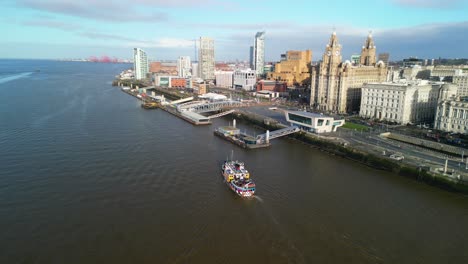 mersey ferry approaching liverpool terminal to dock - tracked by drone from above on a sunny morning, liver buildings backdrop