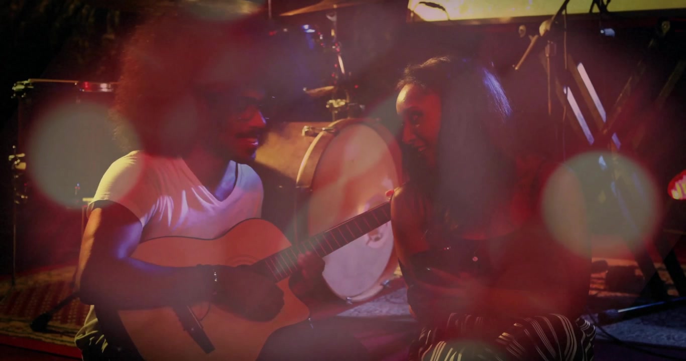 Musicians strumming guitar invoking lens flares while adding shaker percussion synchronizing groove