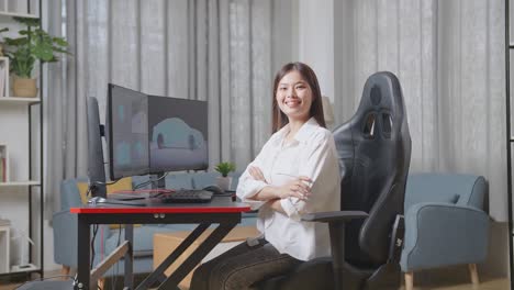 diseñadora automotriz asiática cruzando los brazos y sonriendo a la cámara mientras trabaja en el modelo 3d del coche ev en las computadoras de escritorio en el estudio