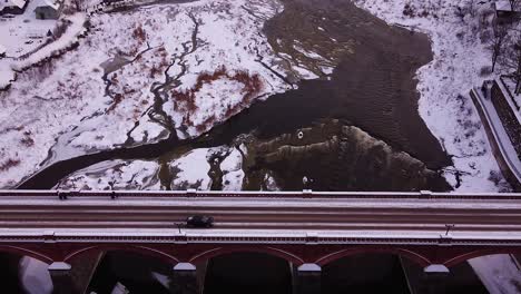 aerial view of old red brick bridge across the venta river in kuldiga, latvia in overcast winter day, venta rapids in background, wide angle revealing drone shot moving backwards