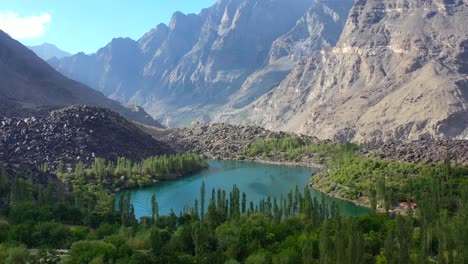 aerial view of turquoise blue water at upper kachura lake surrounded by forest in skardu pakistan on a sunny day with a beautiful large mountain range in the distance