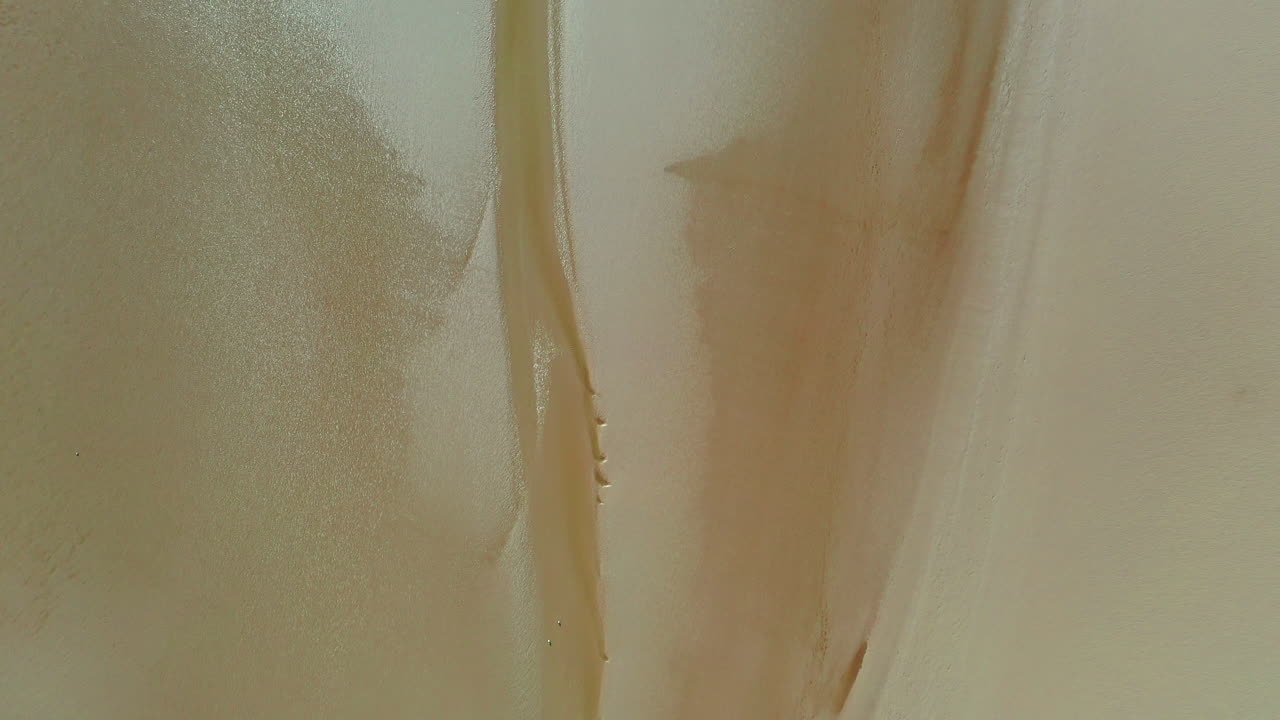 vista aérea de arriba hacia abajo de la arena húmeda dorada, mostrando patrones en la arena, luz del día brillante