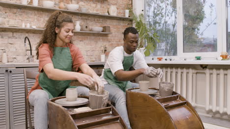 employees wearing green apron modeling ceramic pieces on potter wheel in a workshop while talking to each other